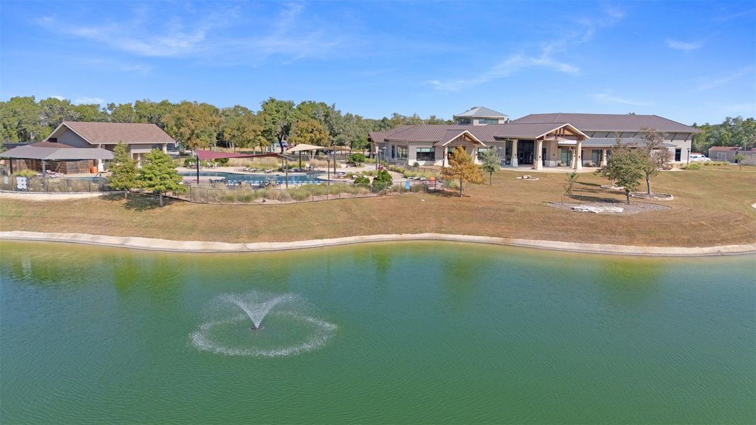 Lush landscaping and serene waters with a fountain frame a welcoming community clubhouse and inviting pool. Lush landscaping and serene waters with a fountain frame a welcoming community clubhouse and inviting pool.