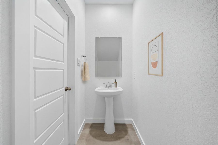 The main-level powder room features a pedestal sink, framed mirror, and neutral finishes making it both inviting and convenient.