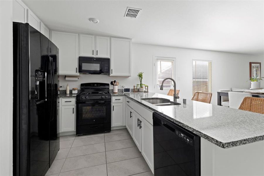 Kitchen with dark stone countertops, black appliances, white cabinets, and a peninsula