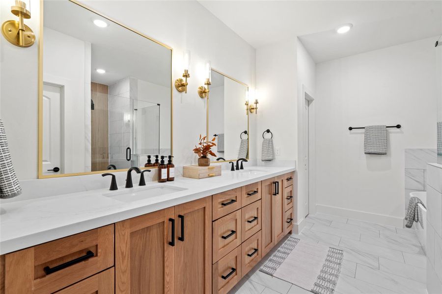 Luxurious primary bathroom featuring a double vanity with quartz countertops, modern matte black fixtures, and elegant gold-accented mirrors - combining warmth and sophistication in one space.