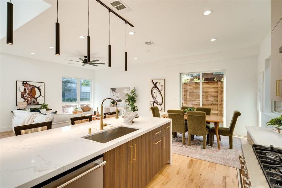 Kitchen featuring sink, light stone countertops, pendant lighting, light wood-type flooring, and appliances with stainless steel finishes