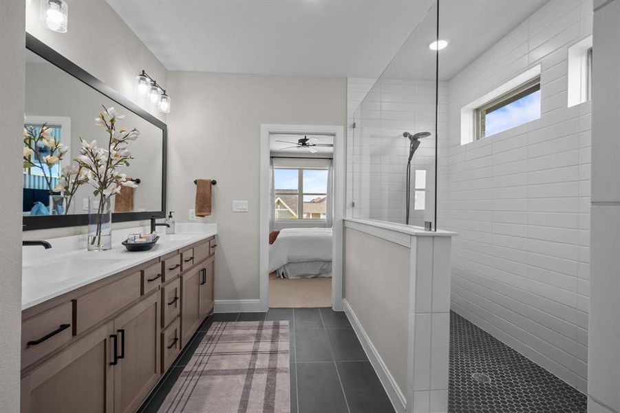 Bathroom featuring connected bathroom, healthy amount of natural light, double vanity, and dark tile patterned floors