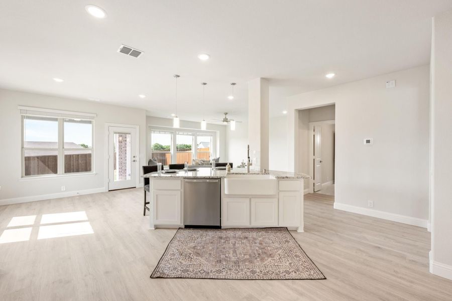 Open-concept kitchen with white cabinets, large island, farmhouse sink, and light hardwood floors