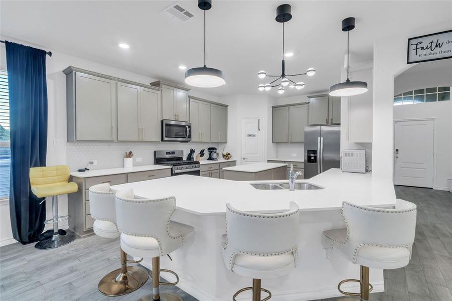 Kitchen with a breakfast bar, appliances with stainless steel finishes, light hardwood / wood-style floors, and hanging light fixtures