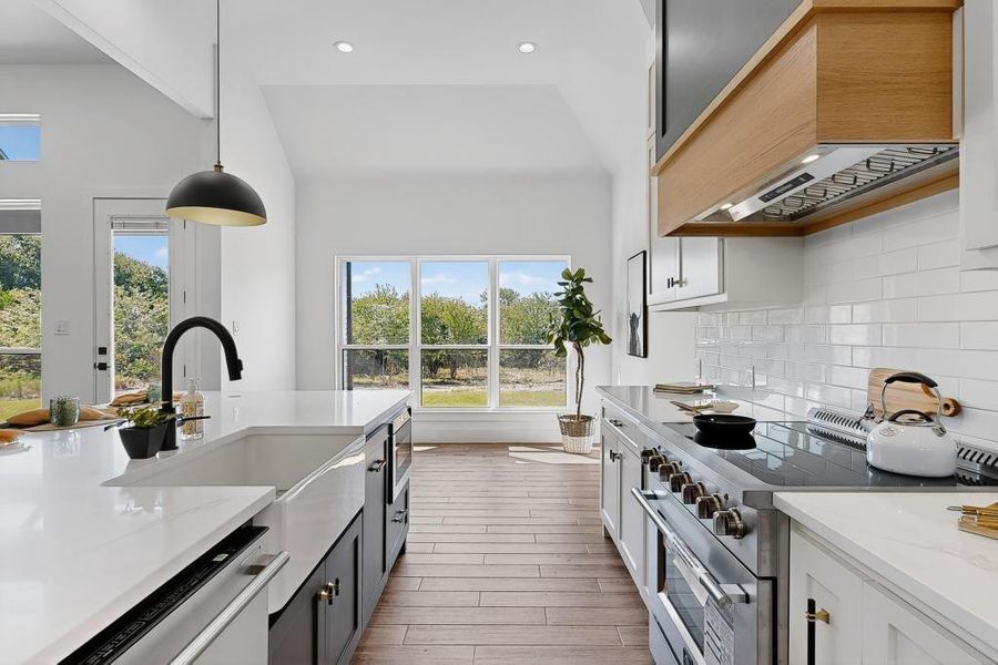 Kitchen with stainless steel stove, wood finished floors, premium range hood, pendant lighting, and decorative backsplash