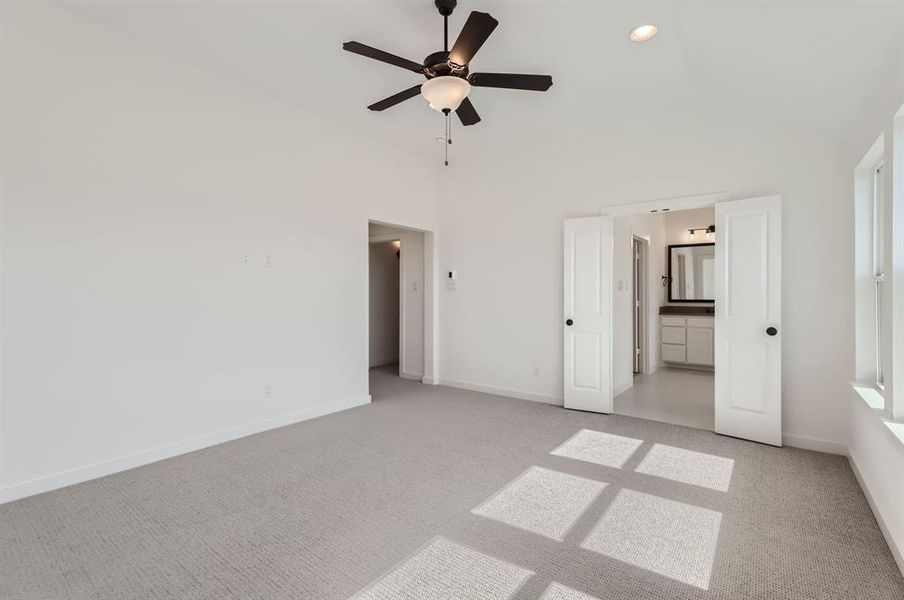 Unfurnished bedroom featuring light carpet, a towering ceiling, ensuite bath, and ceiling fan