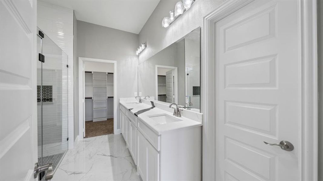 Full bathroom featuring a sink, marble finish floor, a shower stall, double vanity, and a walk in closet