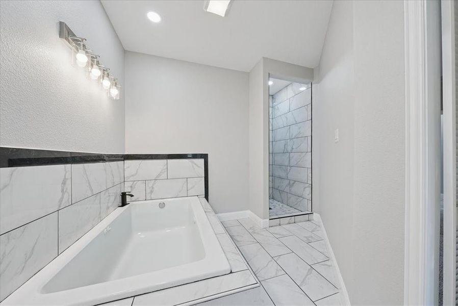 Bathroom featuring a bath, light marble finish floors, recessed lighting, and a walk in shower