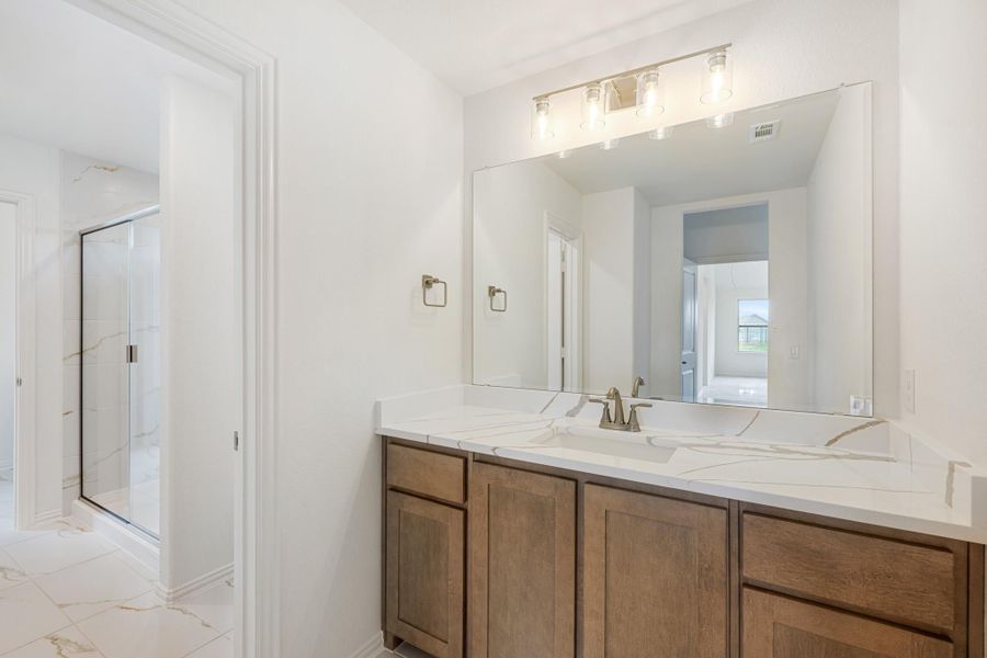 Bathroom vanity with wood cabinets, white quartz countertop, large mirror, and glass shower visible in background. Bathroom vanity with wood cabinets, white quartz countertop, large mirror, and glass shower visible in background.