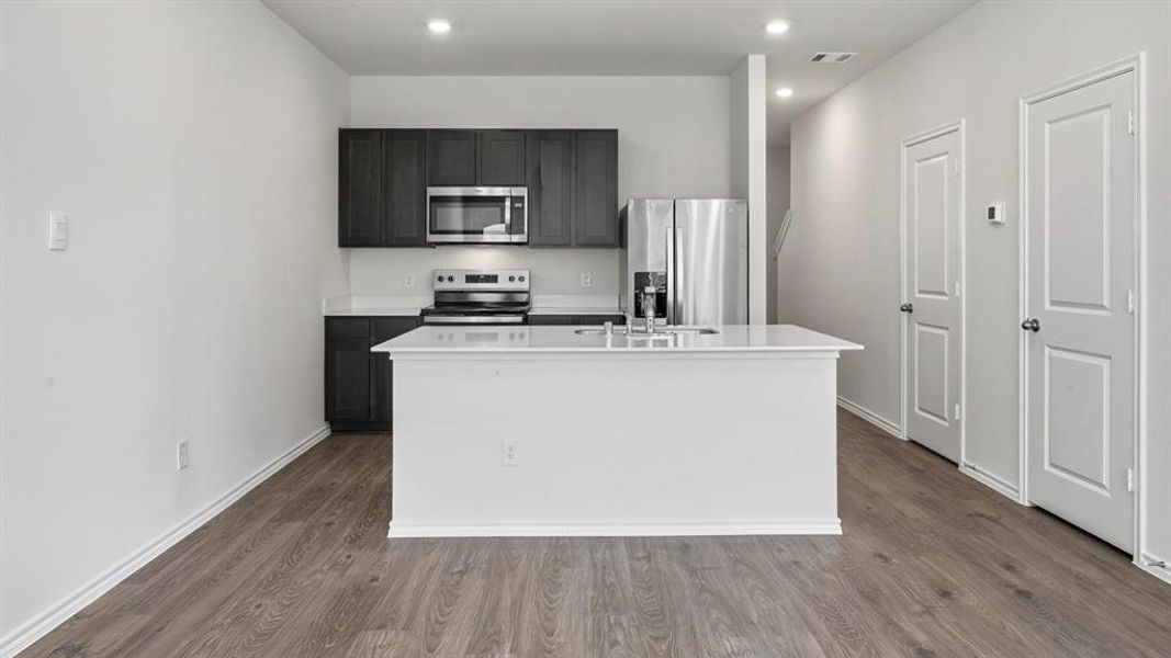 Kitchen featuring appliances with stainless steel finishes, a center island with sink, dark wood-style floors, recessed lighting, and dark cabinetry