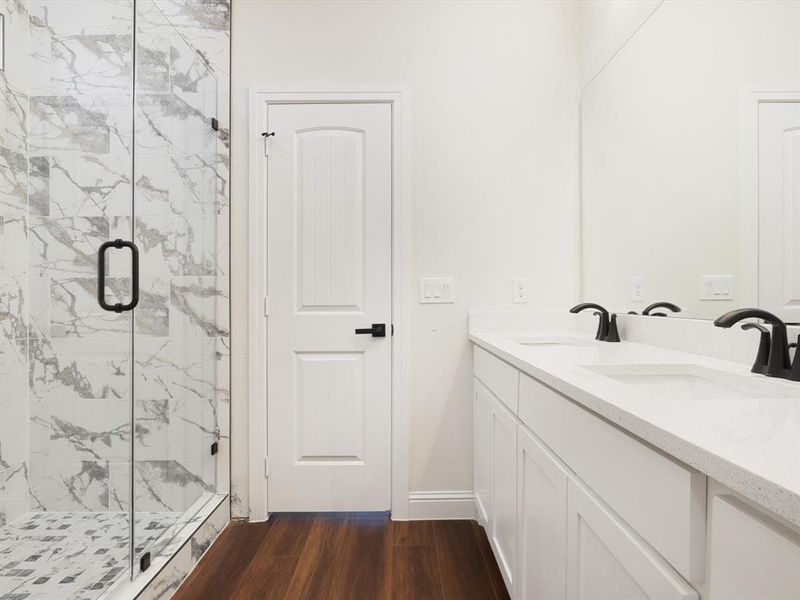 Bathroom featuring a marble finish shower, dark wood-style flooring, and double vanity Bathroom featuring a marble finish shower, dark wood-style flooring, and double vanity