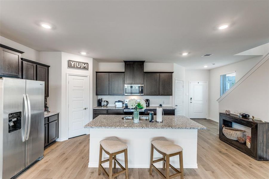Kitchen with appliances with stainless steel finishes, a kitchen breakfast bar, dark brown cabinets, light stone countertops, and recessed lighting Kitchen with appliances with stainless steel finishes, a kitchen breakfast bar, dark brown cabinets, light stone countertops, and recessed lighting