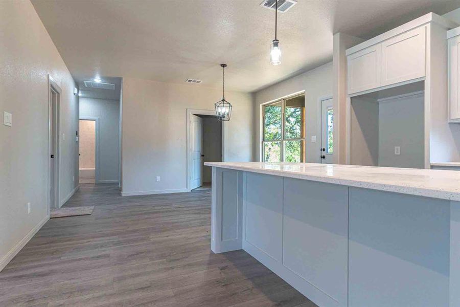 Kitchen featuring light stone counters, dark wood-type flooring, hanging light fixtures, and white cabinets