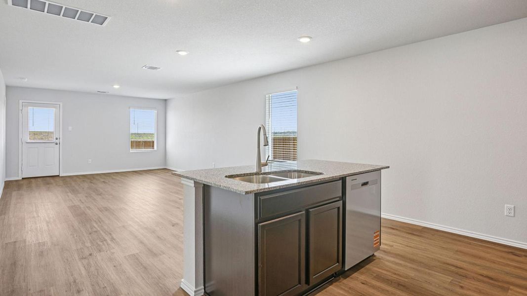 A well-lit kitchen area features a central island with a double sink, seamlessly flowing into a spacious living area.