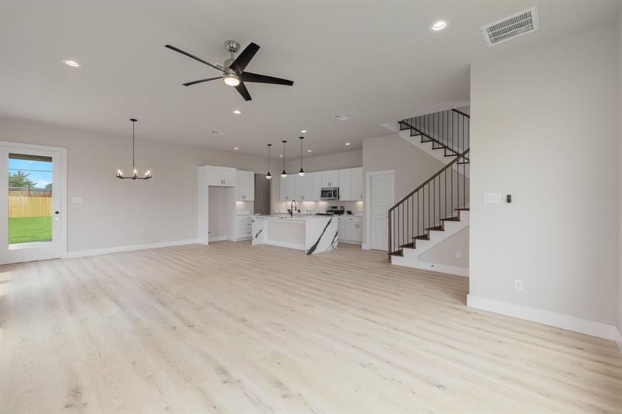 Unfurnished living room featuring light wood-style floors, stairs, a ceiling fan, a chandelier, and baseboards