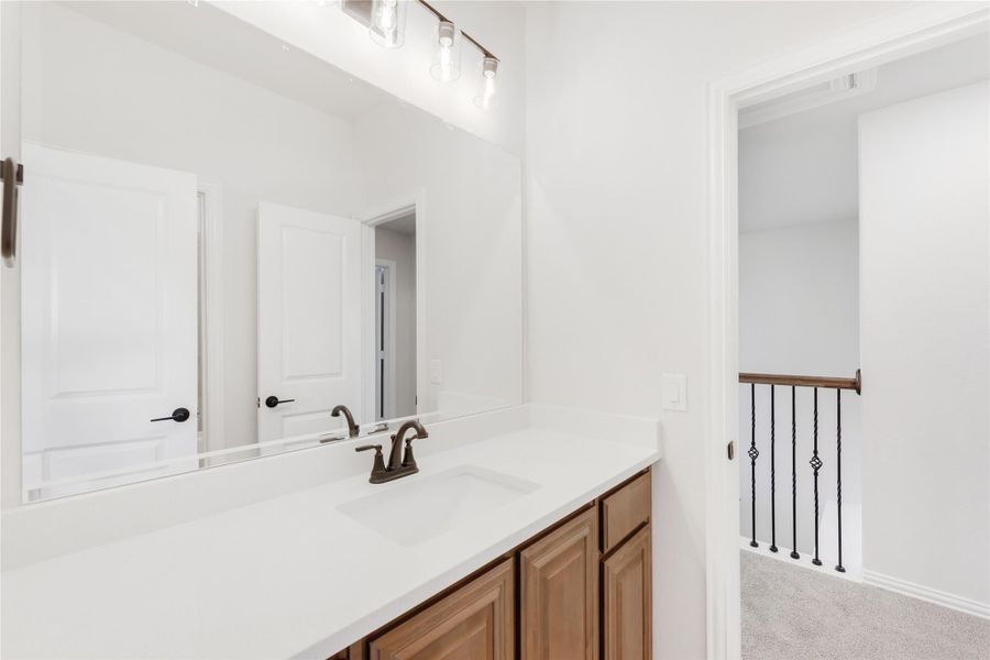 Bathroom vanity with white quartz countertop, wood cabinets, large mirror, and bronze faucet near staircase landing Bathroom vanity with white quartz countertop, wood cabinets, large mirror, and bronze faucet near staircase landing