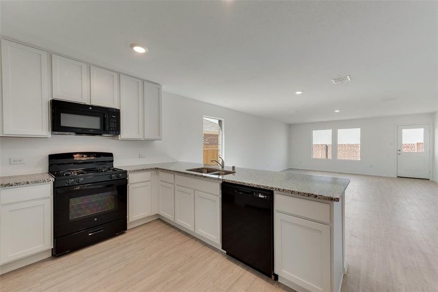 Kitchen with black appliances, kitchen peninsula, white cabinetry, and sink