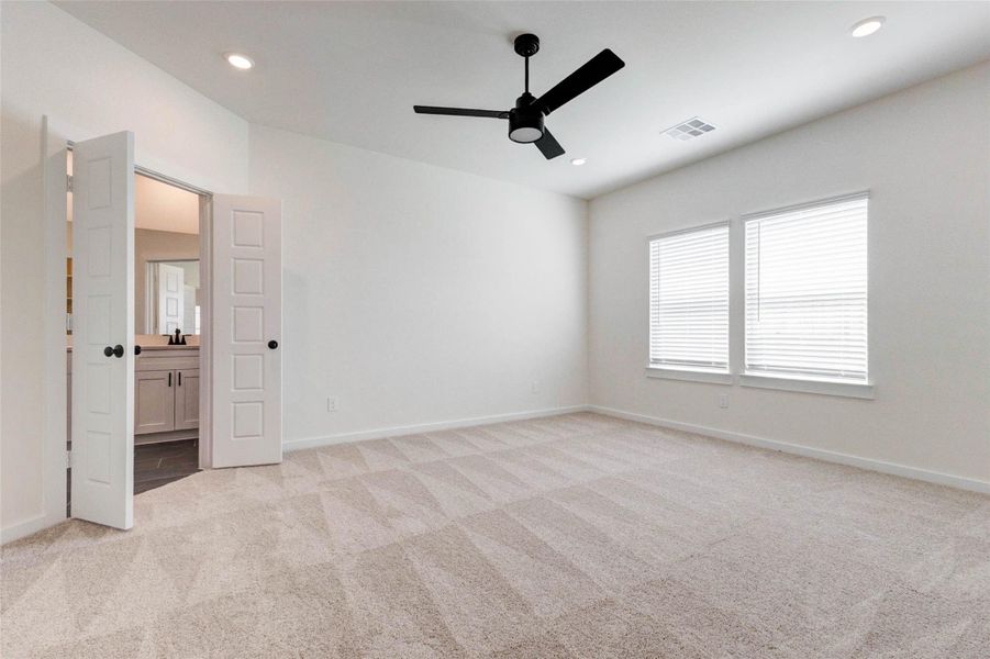 Retreat to this generously sized primary suite featuring plush carpeting, soft neutral tones, and abundant natural light streaming through large windows. The spacious layout easily accommodates oversized furniture, while the modern ceiling fan adds both comfort and style. With direct access to the ensuite bath, this serene bedroom offers the perfect balance of relaxation and functionality.