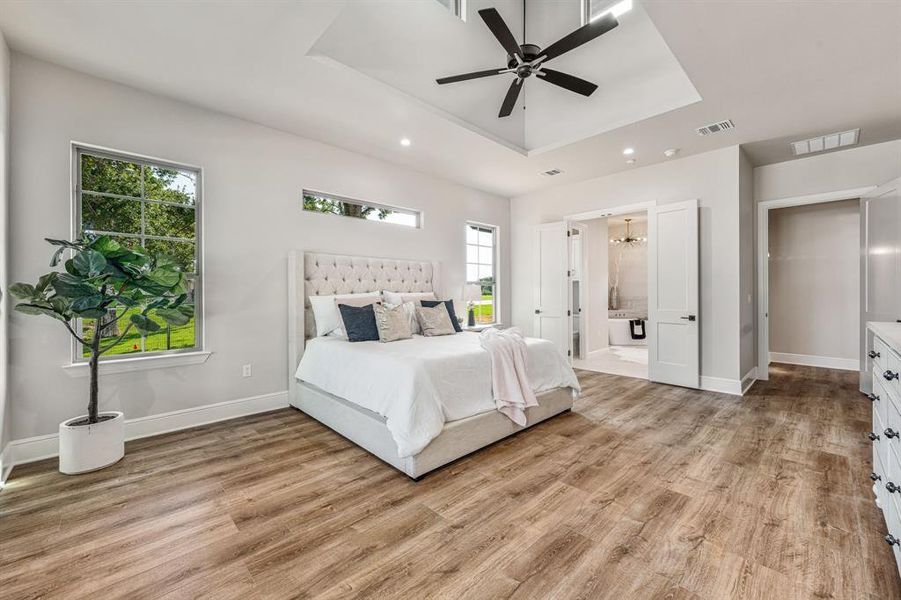 Bedroom with a tray ceiling, light wood-type flooring, and ceiling fan