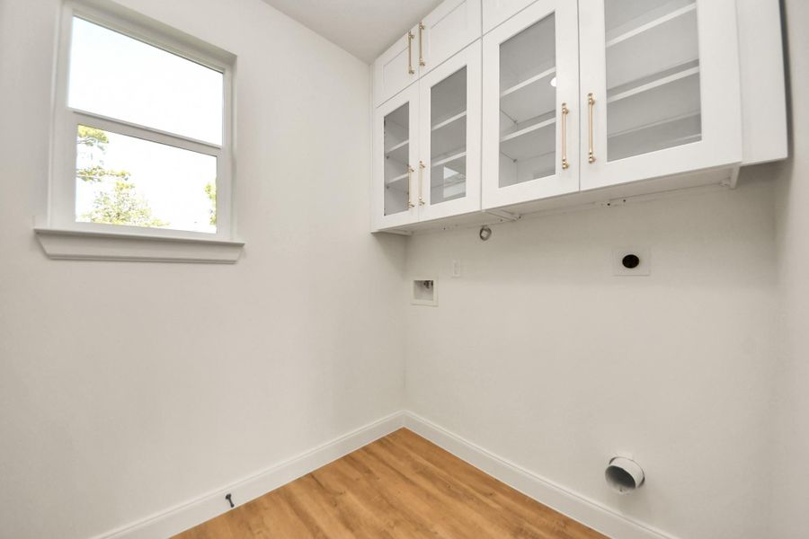 This bright laundry room features white cabinetry with glass doors, and a window for natural light. It has hookups for a washer and dryer. This bright laundry room features white cabinetry with glass doors, and a window for natural light. It has hookups for a washer and dryer.