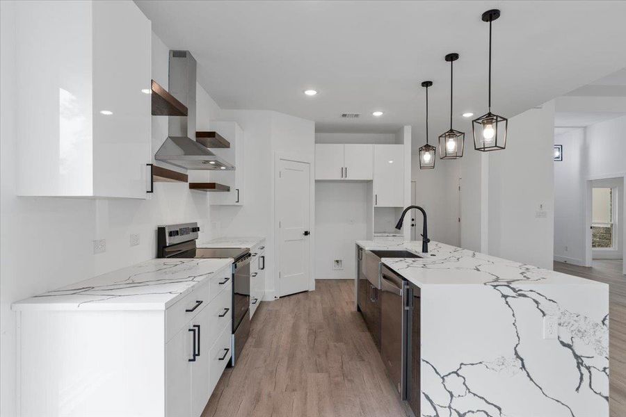 Kitchen featuring appliances with stainless steel finishes, wall chimney exhaust hood, modern cabinets, light wood finished floors, and white cabinets Kitchen featuring appliances with stainless steel finishes, wall chimney exhaust hood, modern cabinets, light wood finished floors, and white cabinets