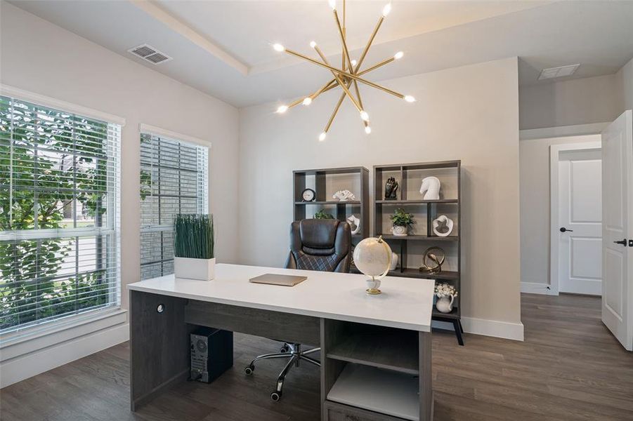 Dedicated office space featuring wood-finish flooring, two large windows with blinds, a modern sputnik chandelier, two built-in shelving units, and a recessed ceiling detail