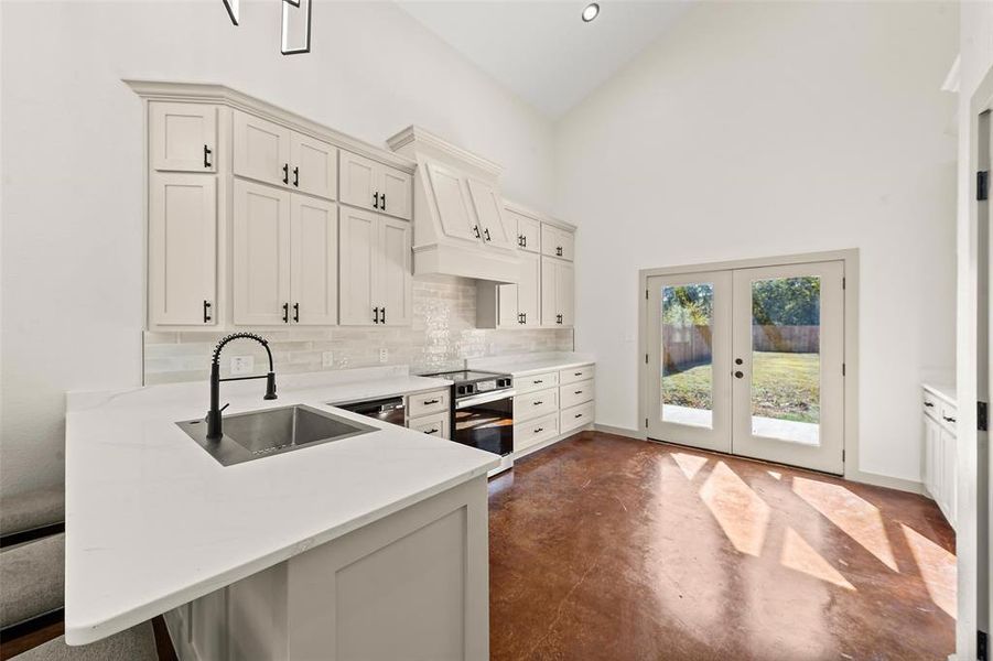Kitchen with tasteful backsplash, finished concrete flooring, range with electric stovetop, high vaulted ceiling, and french doors