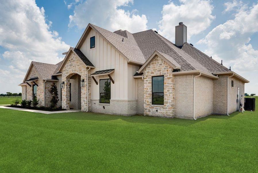 View of front of property featuring board and batten siding, a shingled roof, a front lawn, stone siding, and a chimney