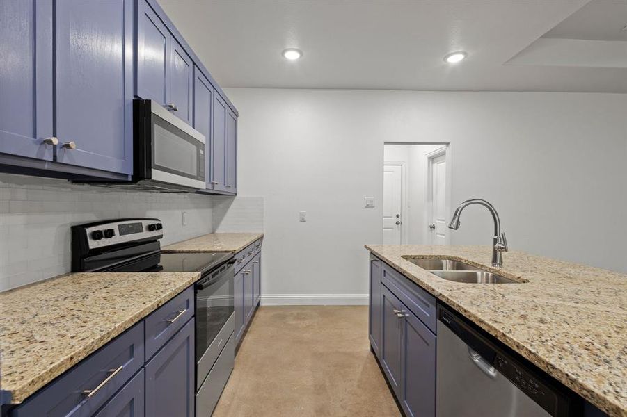 Kitchen with sink, blue cabinetry, appliances with stainless steel finishes, light stone counters, and tasteful backsplash