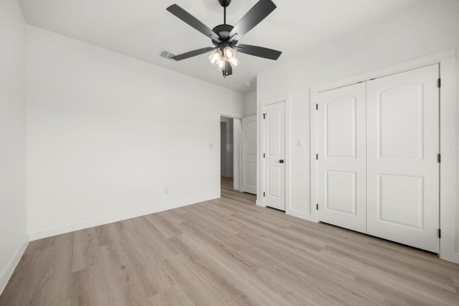 A quiet bedroom featuring light wood-look flooring and a modern ceiling fan for comfort. A quiet bedroom featuring light wood-look flooring and a modern ceiling fan for comfort.