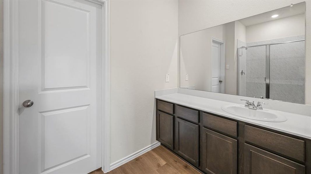 Bathroom vanity featuring a single sink set in a light-colored countertop, dark wood-finish cabinetry, a large wall-mounted mirror, and wood-finish flooring