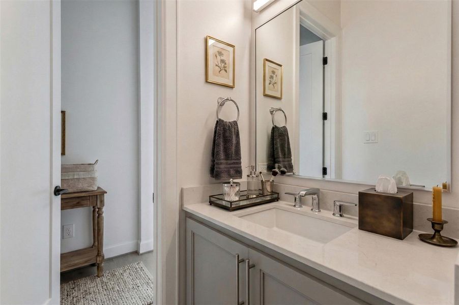 Elegant second-floor powder bath featuring a Quartz countertop, undermount sink, sleek chrome fixtures, and clean-lined cabinetry with modern hardware. An oversized mirror enhances light and visual space. Conveniently located off the main living area, this half bath adds functionality while maintaining the home’s cohesive upscale finishes. This photo has been virtually staged for visual reference.