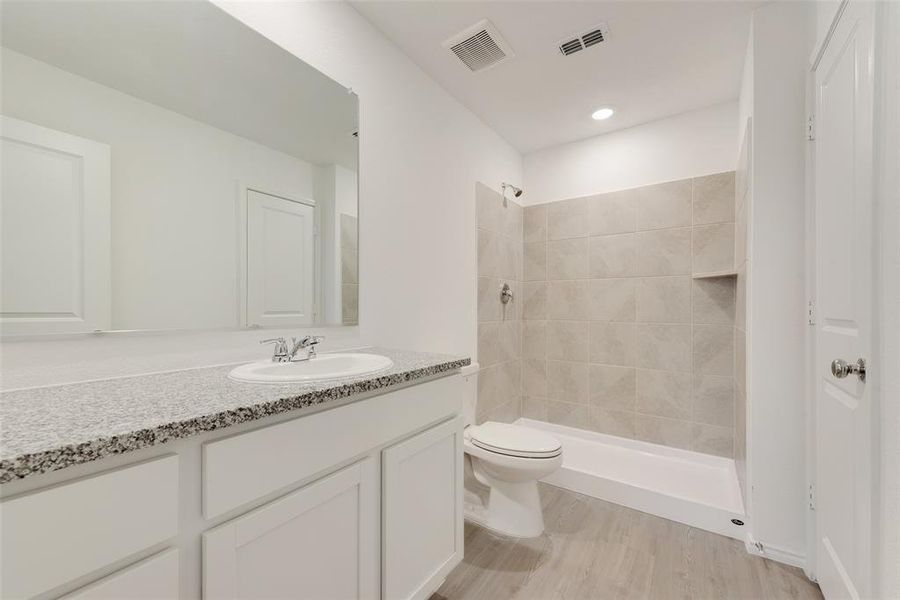 Bathroom with vanity, hardwood / wood-style floors, toilet, and tiled shower