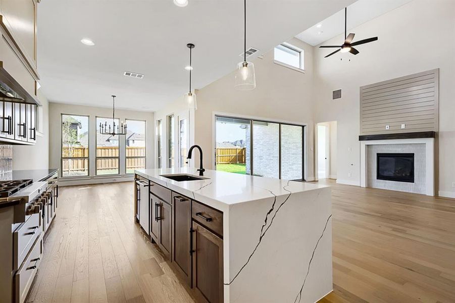 Kitchen featuring open floor plan, light stone countertops, light wood-style flooring, an island with sink, and vaulted ceiling Kitchen featuring open floor plan, light stone countertops, light wood-style flooring, an island with sink, and vaulted ceiling