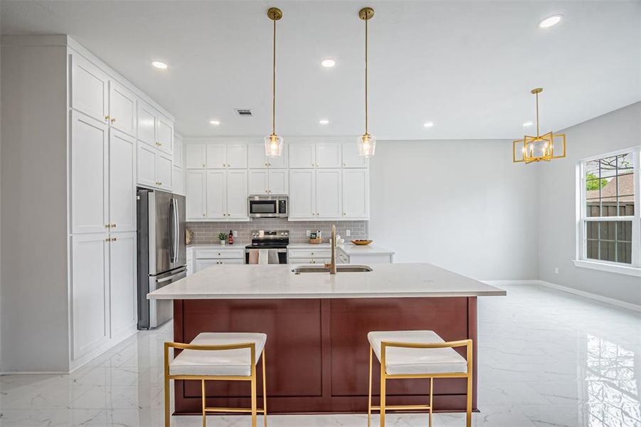 Kitchen featuring stainless steel appliances, light marble finish floors, a kitchen island with sink, a breakfast bar area, and light stone counters