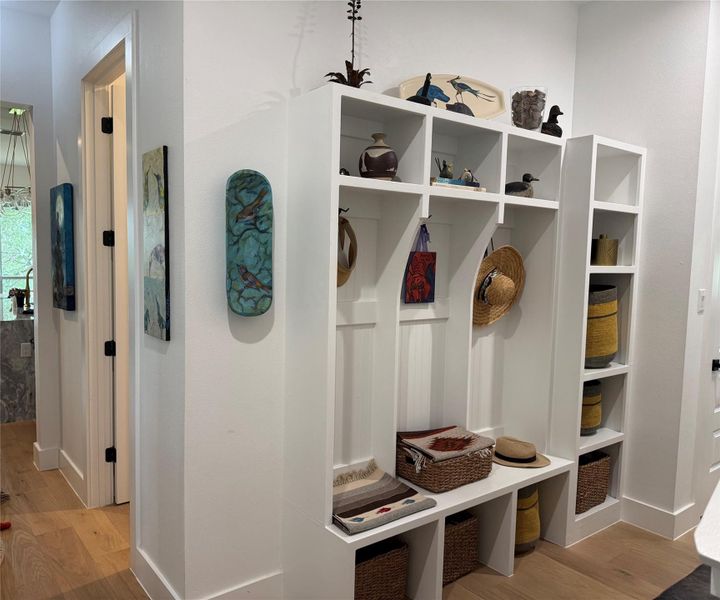 Custom built-in entryway storage with bench seating, individual cubbies, and integrated shelving, complemented by light wood-finish flooring