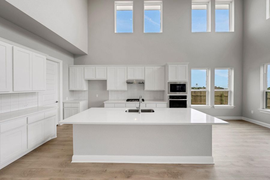 Kitchen featuring backsplash, black oven, white cabinets, light wood finished floors, and a towering ceiling Kitchen featuring backsplash, black oven, white cabinets, light wood finished floors, and a towering ceiling