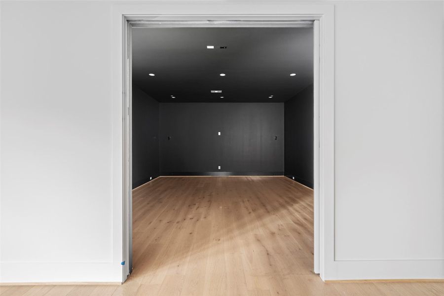 A dedicated media room offers a dramatic, theater-style setting with dark walls, recessed lighting, and warm wood flooring.