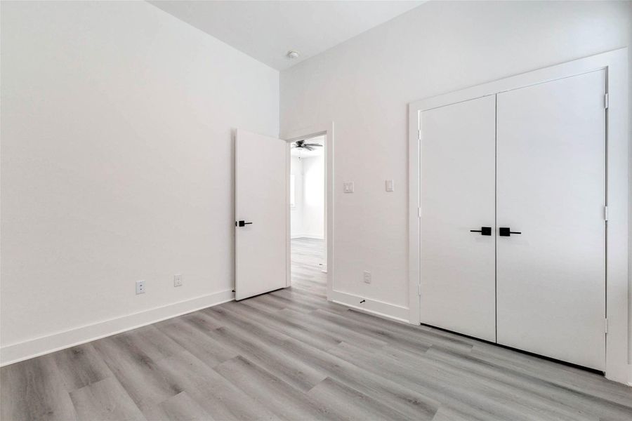 This bright bedroom offers a calm neutral palette, durable gray-toned plank flooring, high ceilings, and a generous double-door closet. Crisp white walls and contrasting black hardware create a modern canvas ready for personalized style. This bright bedroom offers a calm neutral palette, durable gray-toned plank flooring, high ceilings, and a generous double-door closet. Crisp white walls and contrasting black hardware create a modern canvas ready for personalized style.