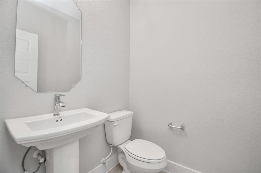 Immerse yourself in modern elegance within this delightful half bathroom. Featuring a sophisticated 5-panel door, upgraded pedestal sink, contemporary hardware,  it exudes a sense of refinement. Sample photo of completed home. Actual colors and selections will vary.