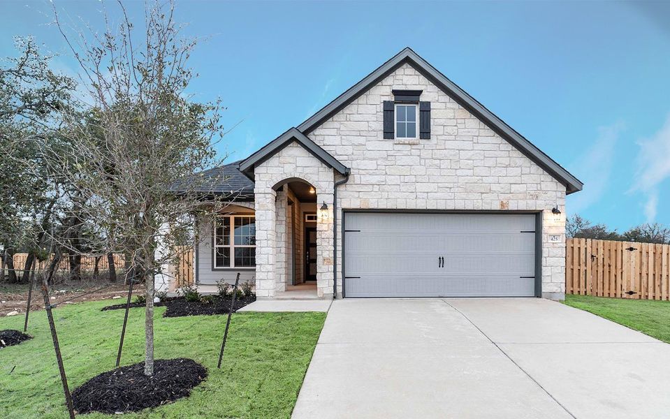 French country inspired facade with a front yard, fence, a garage, stone siding, and driveway