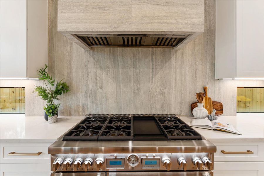 Commercial grade 48-inch Thermador range delivers restaurant-quality performance with its impressive double oven setup, six precision burners, and integrated griddle.  The powerful Thermador ventilation system is beautifully concealed within a custom decorative hood featuring elegant fluted stone that seamlessly matches the kitchen backsplash.