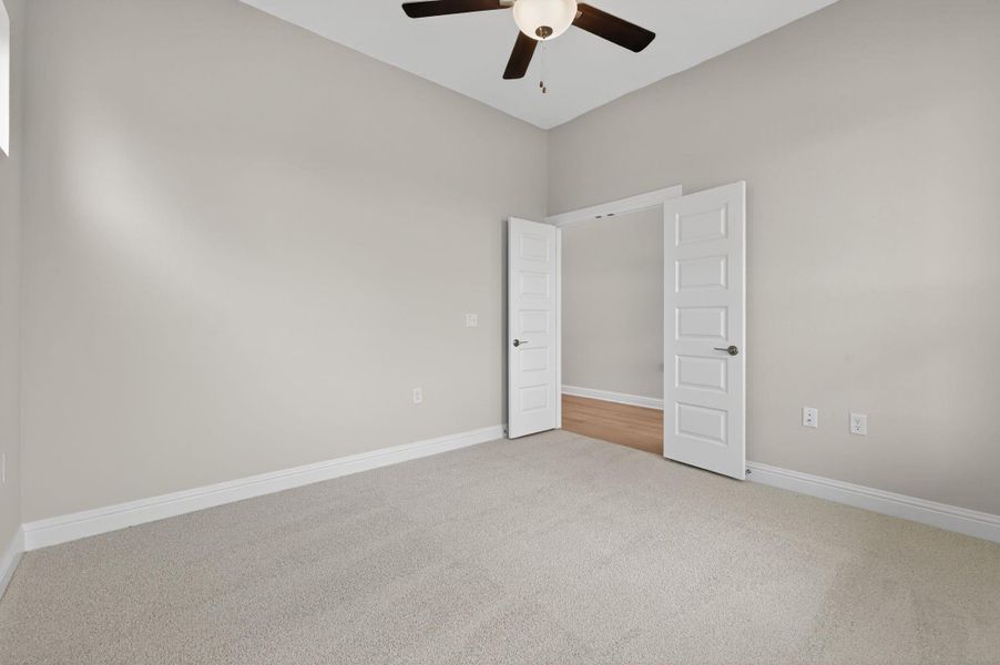 Empty room with light colored carpet and a ceiling fan
