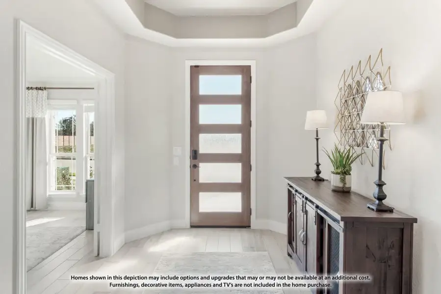 Bright home entryway with wood and glass front door, tray ceiling, and dark wood console table with lamps.