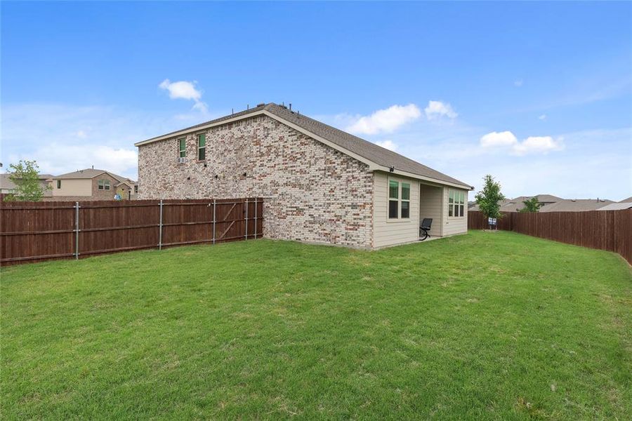 Spacious backyard featuring a manicured lawn, full privacy fencing, and a covered patio area