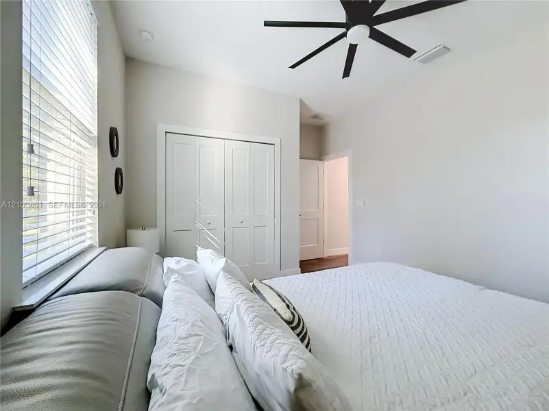 Neutral interior featuring high ceilings, a multi-blade matte black ceiling fan, white paneled closet doors, and horizontal slat window blinds