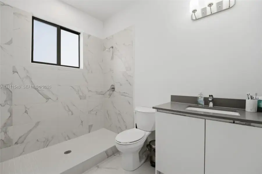 Bathroom featuring a walk-in shower with large-format stone-patterned tile, a vanity with a solid-surface countertop and integrated sink, and wall-mounted vanity lighting