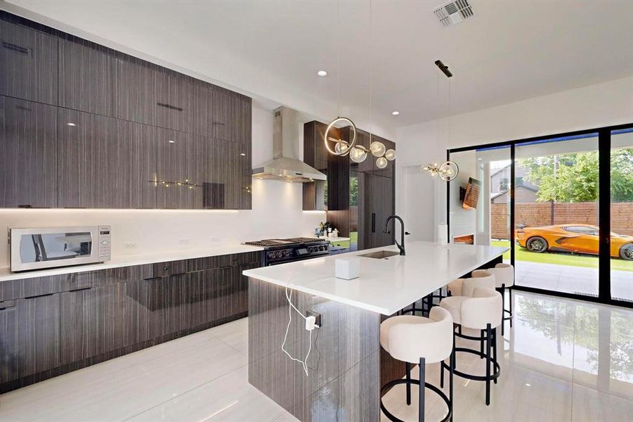Kitchen with wall chimney exhaust hood, white microwave, modern cabinets, a kitchen bar, and light tile patterned floors Kitchen with wall chimney exhaust hood, white microwave, modern cabinets, a kitchen bar, and light tile patterned floors