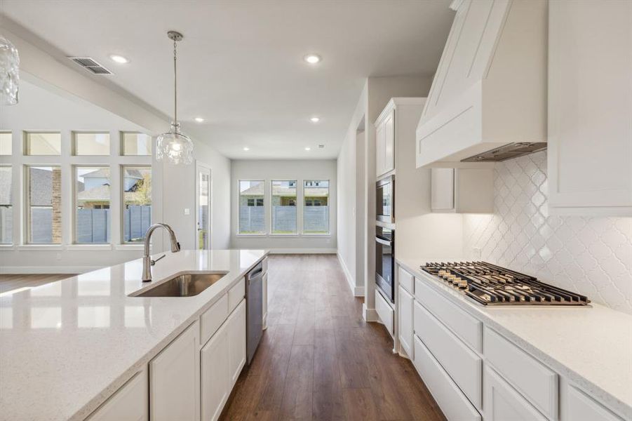 Kitchen with sink, stainless steel appliances, pendant lighting, dark wood-type flooring, and premium range hood