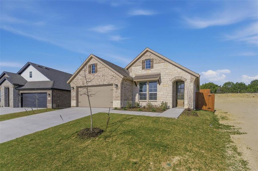 French country inspired facade with driveway, a front lawn, a garage, stone siding, and brick siding